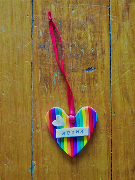 Christmas tree decoration, a heart made with rainbow colours, and the word 'Aroha' on the front, tied with a red ribbon