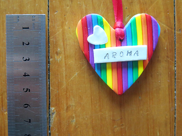 Christmas tree decoration, a heart made with rainbow colours, and the word 'Aroha' on the front, measures approx 5cm